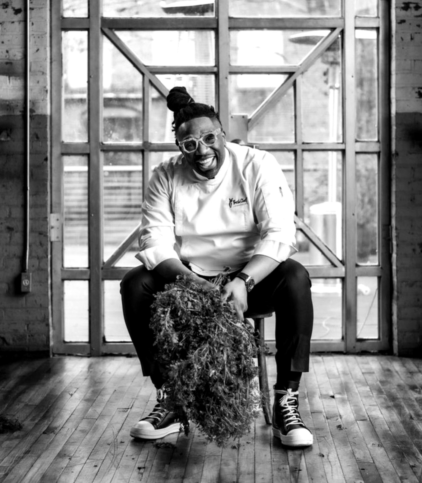 Chef Ameer Natson, founder of Fresh Chef Foundation, seated in an industrial loft holding a large bundle of fresh greens